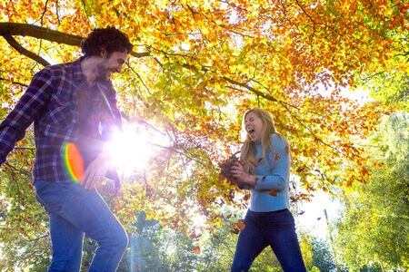 Young couple having fun in Autumn. They are throwing leaves at each other under the trees.