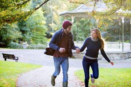 Young couple running togerther through a park in Autumn.の写真素材