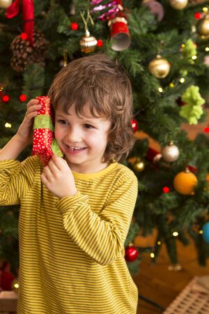 Little boy shaking a present close to his ear to try and guess what it is. He is standing in front of the Christmas tree.の写真素材