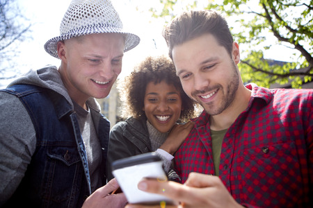 Three friends looking at a smart phone together outdoors.の写真素材