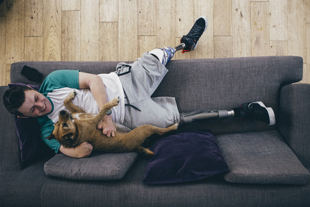 Quadruple amputee relaxing on the sofa at home with his dog.の写真素材