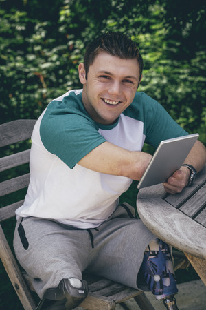 Quadriplegic man sitting in his garden with a digital tablet. He is smiling at the camera.の写真素材