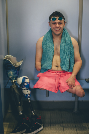 Quadriplegic swimmer in the changing cubicle. He is smiling for the camera with his prosthetic legs next to him.の写真素材