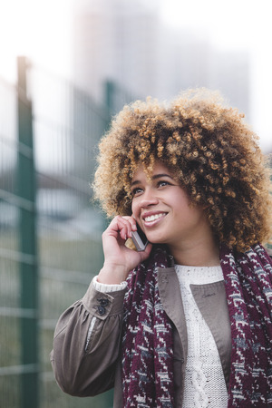 Woman talking on the phone outdoors. It is foggy and she is wearing warm clothing.の写真素材