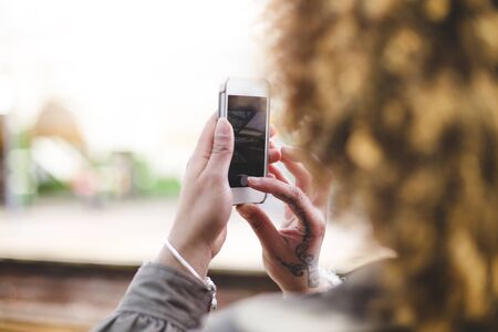 Over the shoulder shot of a woman using a smart phone to take a photo at a train station.の写真素材