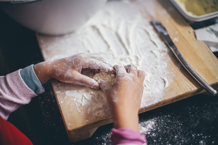 Close up of a little girl kneading dough on a wooden board .の写真素材
