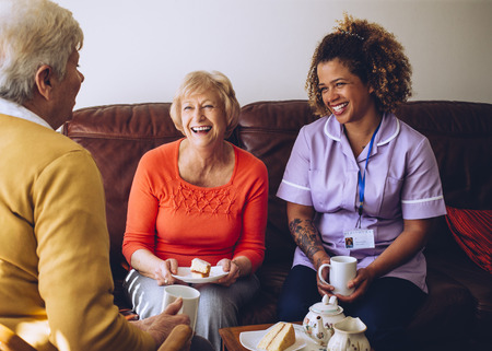 Elderly carer sitting with two of her patients in the care home. They are enjoying some cake and tea.の写真素材