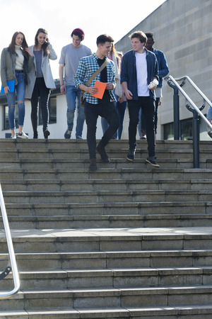 A group of students laugh and smile as they leave one of their lectures. They are walking down some steps carrying their books, bags and digital tablets.の写真素材