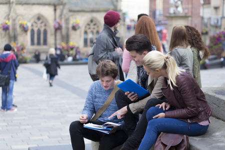 A group of young students smile as they study together outdoors. They are looking at eachother's notes on their notepads and a digital tablet.の写真素材