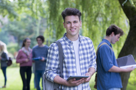 Portrait of a teenage boy on a school trip. He is holding a digital tablet and smiling at the camera.の写真素材