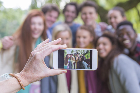 A happy group of students smile at the camera as someone takes an image of them on a mobile phone. The phone is being held by a mother taking an image of them going back to college.の写真素材