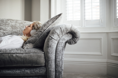 Mature woman lying on her sofa, enjoying listening to some music through headphones.の写真素材
