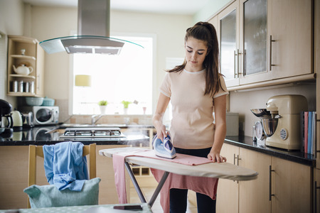 Teenage girl ironing laundry in the kitchen.の写真素材