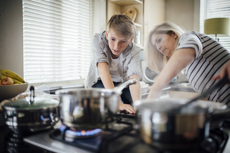 Mother and son cooking dinner together in the kitchen. They are cooking vegetables on the hob.の写真素材