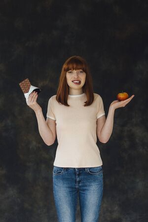 Woman standing against a studio background with an apple and a chocolate bar in each hand.の写真素材