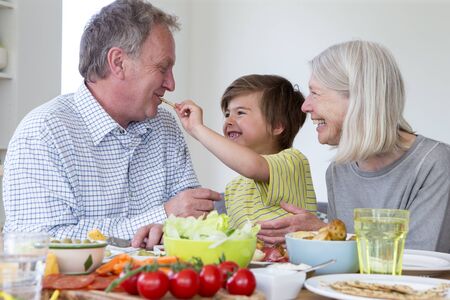 Little boy is feeding his grandfather a cream cracker while having a mediterranean style lunch with...