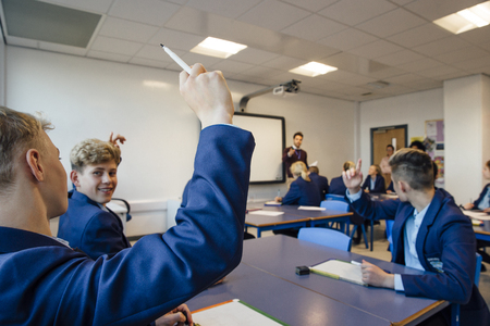 Point of view shot of a high school lesson where the teacher has asked a question and some students have their hands up to answer.の写真素材