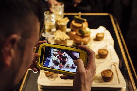 Man is taking a photo of his meal in a restaurant using his smart phone.