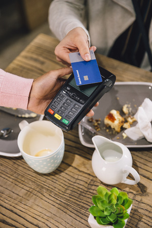 High angle view of a woman making a contactless card payment for her coffee and scone in a cafe. の写真素材