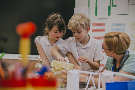 Primary school students are working on an arts and crafts project with their teacher. They are taping sponges together into a shape.の写真素材