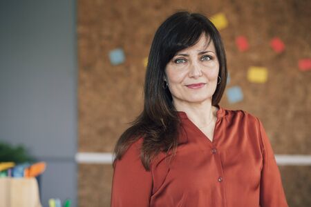 Portrait of a mature, female business owner in her office. She is standing in front of a cork board and is smartly dressed, smiling for the camera.の写真素材
