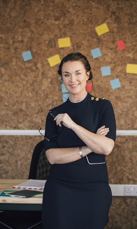 Portrait of a beautiful woman in her workplace. She is standing in front of a corkboard and is smartly dressed, smiling for the camera.の写真素材