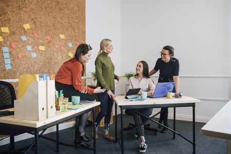 Women are working together in an office. They are talking as they use technology.の写真素材