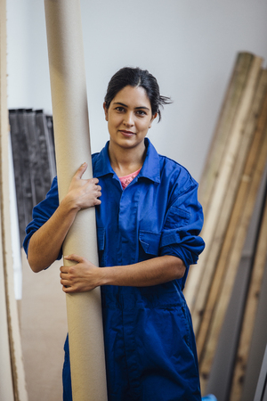 Portrait of a female carpenter at work. She is holding a cardboard tube and is smiling for the camera.の写真素材