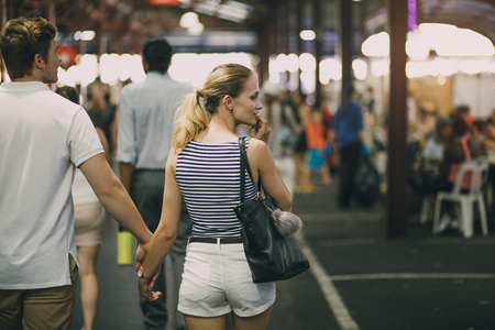Young couple are exploring Queen Victoria Market in Australia. They are holding hands and the woman is looking out oft he frame to something she is tempted to buy.の写真素材