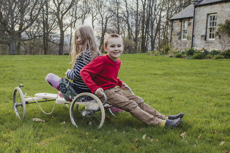 Siblings are posing for the camera while sitting on a go kart in the garden.の写真素材