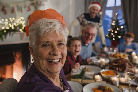 Happy grandmother at a family christmas dinner. She is smiling for the camera while wearing a...