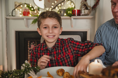 Happy little boy is smiling for the camera while sitting at the table for christmas dinner.