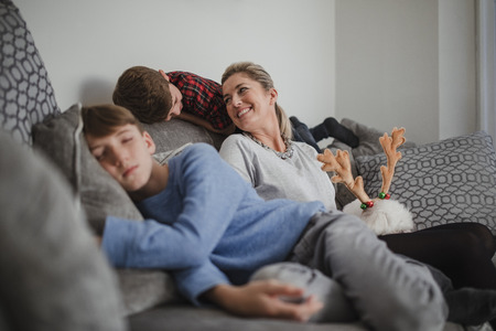 Mother is relaxing with her two sons and her pet dog on the sofa at home.の写真素材
