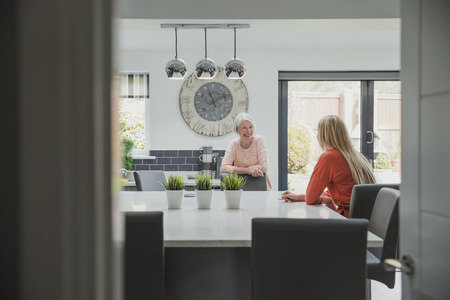 Senior woman is enjoying a catch up with her daughter. They are in the kitchen of her home.の写真素材