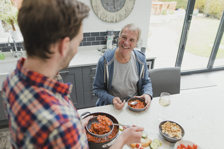 Mature man is enjoying a meal at home with his son.の写真素材