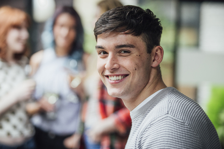 Portrait of a young man at a social gathering in a bar courtyard. He is smiling at the camera.の写真素材
