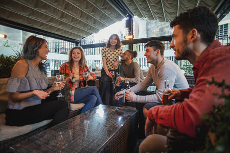 Group of friends are enjoying drinks as they chat in a bar courtyard.の写真素材