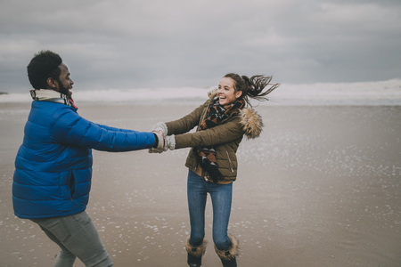 A young couple laugh and dance on Tynemouth beach in winter.の写真素材