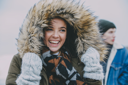 A woman laughing on a winter beach with an out of focus male in the background.の写真素材