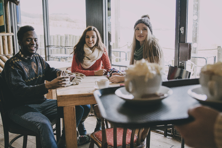 A group of teenagers happy to see their coffee being served in a cafe in winter.の写真素材