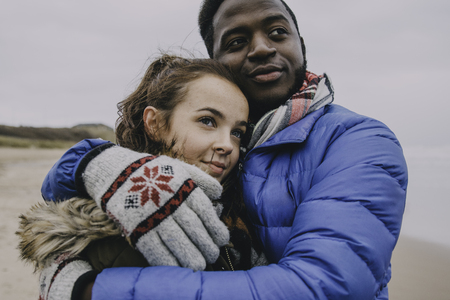 A young couple hug and look into the distance on a winter beach.の写真素材