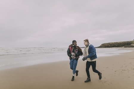 Two friends talk and laugh whilst walking along a winter beach.の写真素材