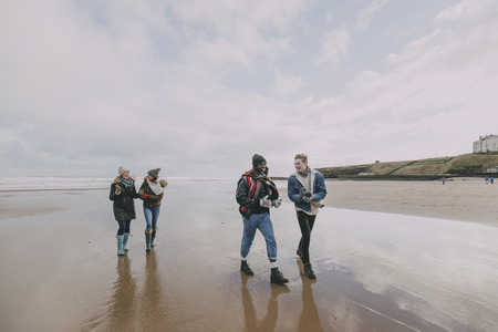 A group of teenagers talk and laugh together whilst walking along a winter beach.の写真素材
