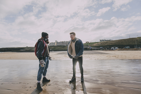 Two young adults stand and talk on a winter beach in Tynemouth.の写真素材