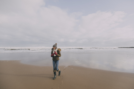 A young woman walks alone along a winter beach in Tynemouth whilst smiling.の写真素材