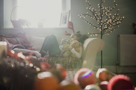 Little girls are lying down after a busy christmas morning. One is wearing christmas antlers and cuddling teddybears.の写真素材