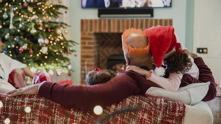 Father is curled up on the sofa ith his daughter at christmas time, watching television.の写真素材