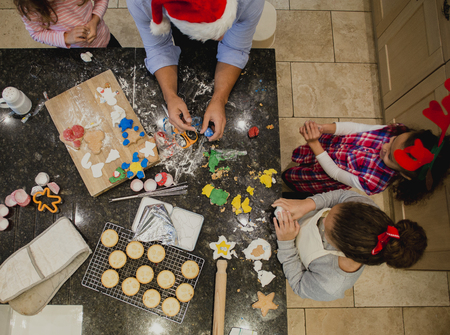 Aerial view of a father making christmas biscuits with his three daughters in the kitchen of their home. They are making festive shapes and covering them in icing.の写真素材
