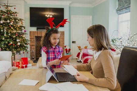 Little girl is making and writing out christmas cards with her mother at the dining table in their home.の写真素材