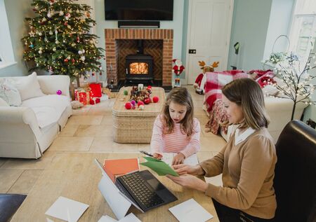 Little girl is making and writing out christmas cards with her mother at the dining table in their home.の写真素材